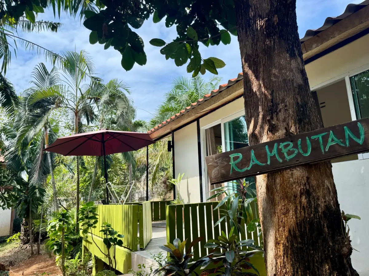 Exterior of Rambutan House with hand-painted wooden sign, green fence and tropical garden on Koh Mak