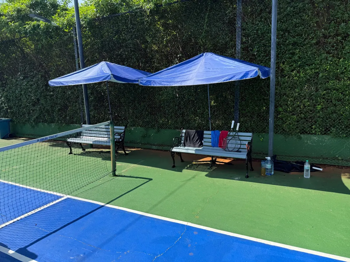 Shaded benches beside the blue tennis court at Koh Mak Sports Village