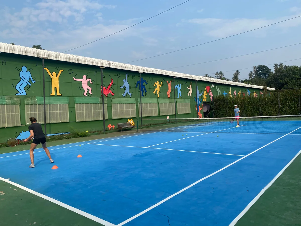 Tennis players on a bright blue court with colourful mural at Phoenix Gym Koh Mak