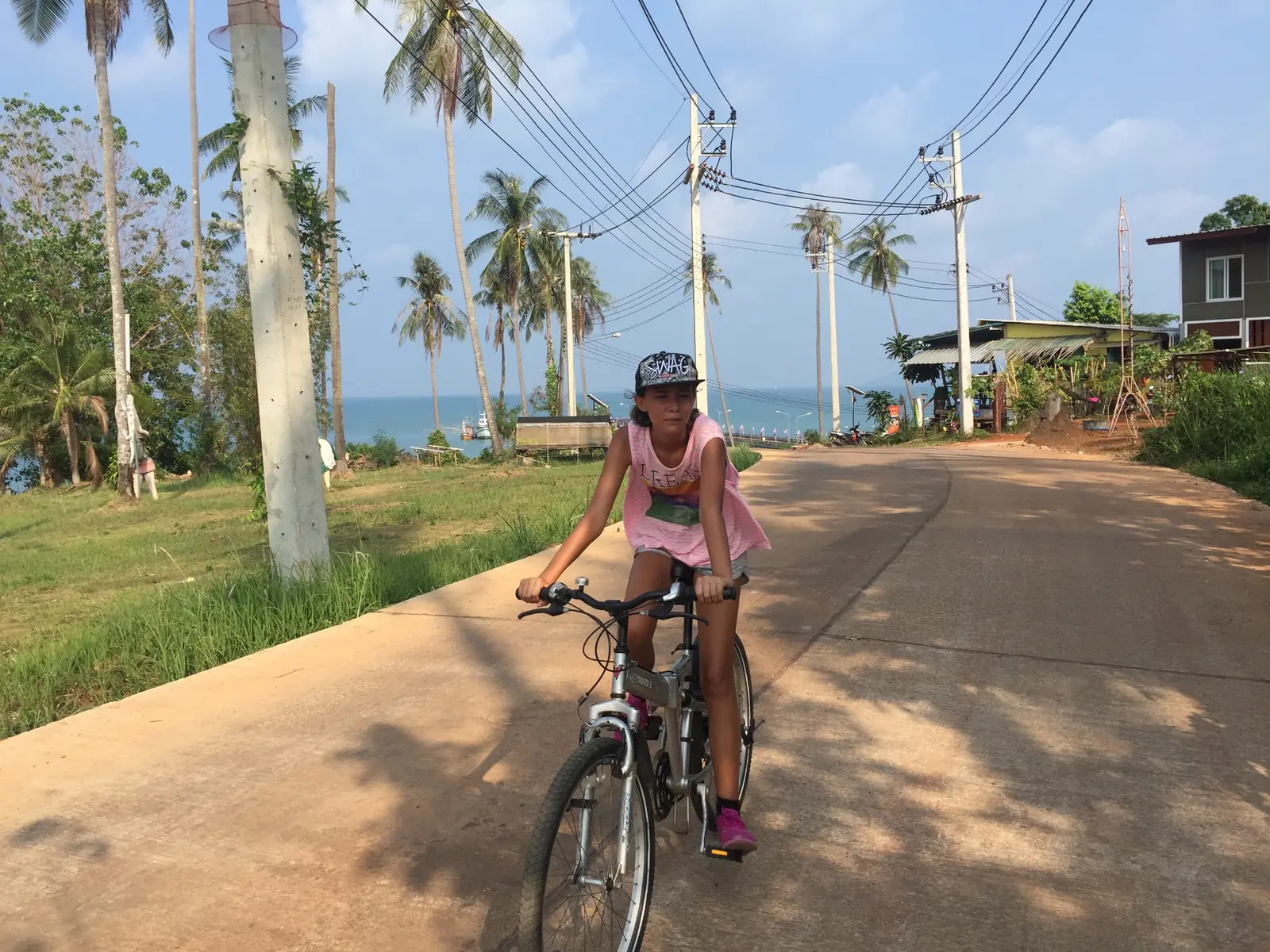 Cyclist riding along a coastal road lined with palm trees on Koh Mak