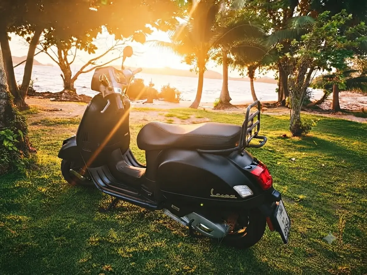 Classy black Vespa scooter parked on grass near a Koh Mak beach at sunset