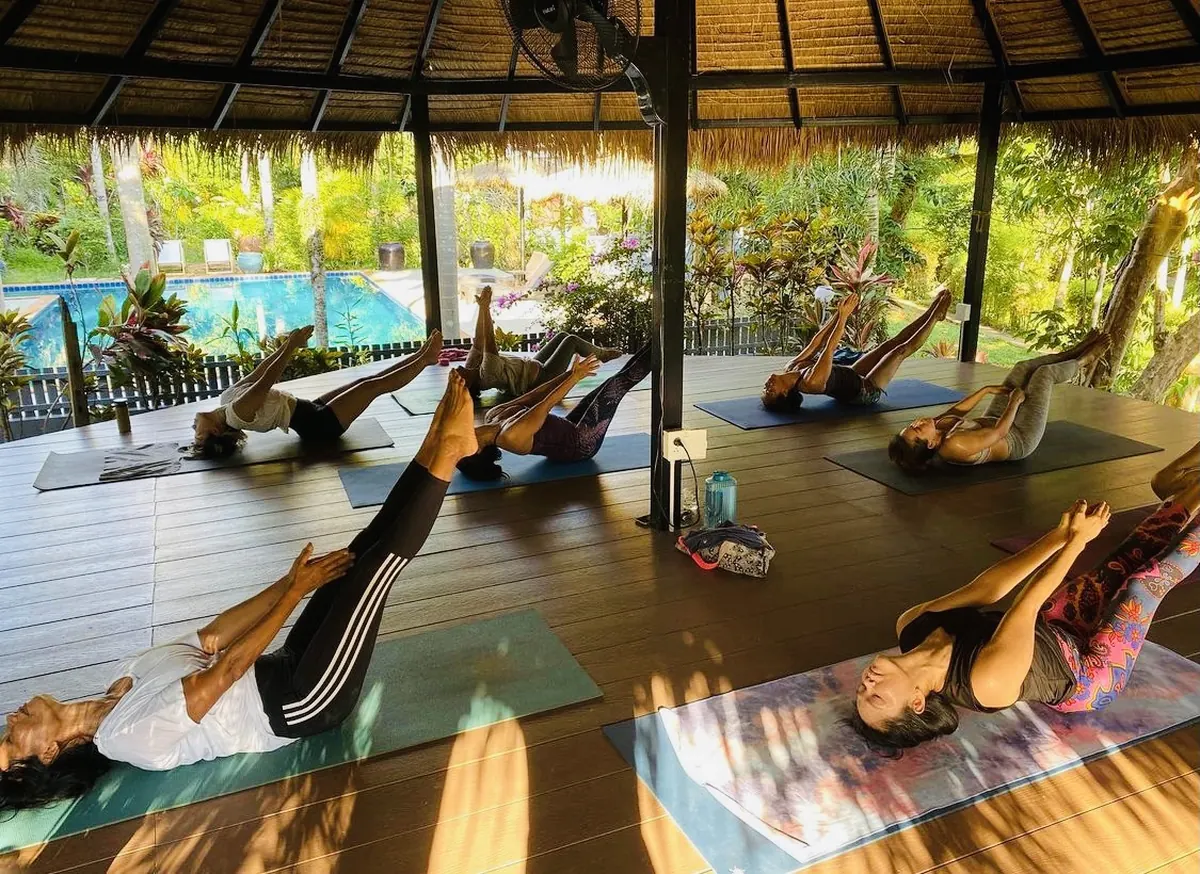Yoga class on mats in an open thatched pavilion overlooking the pool
