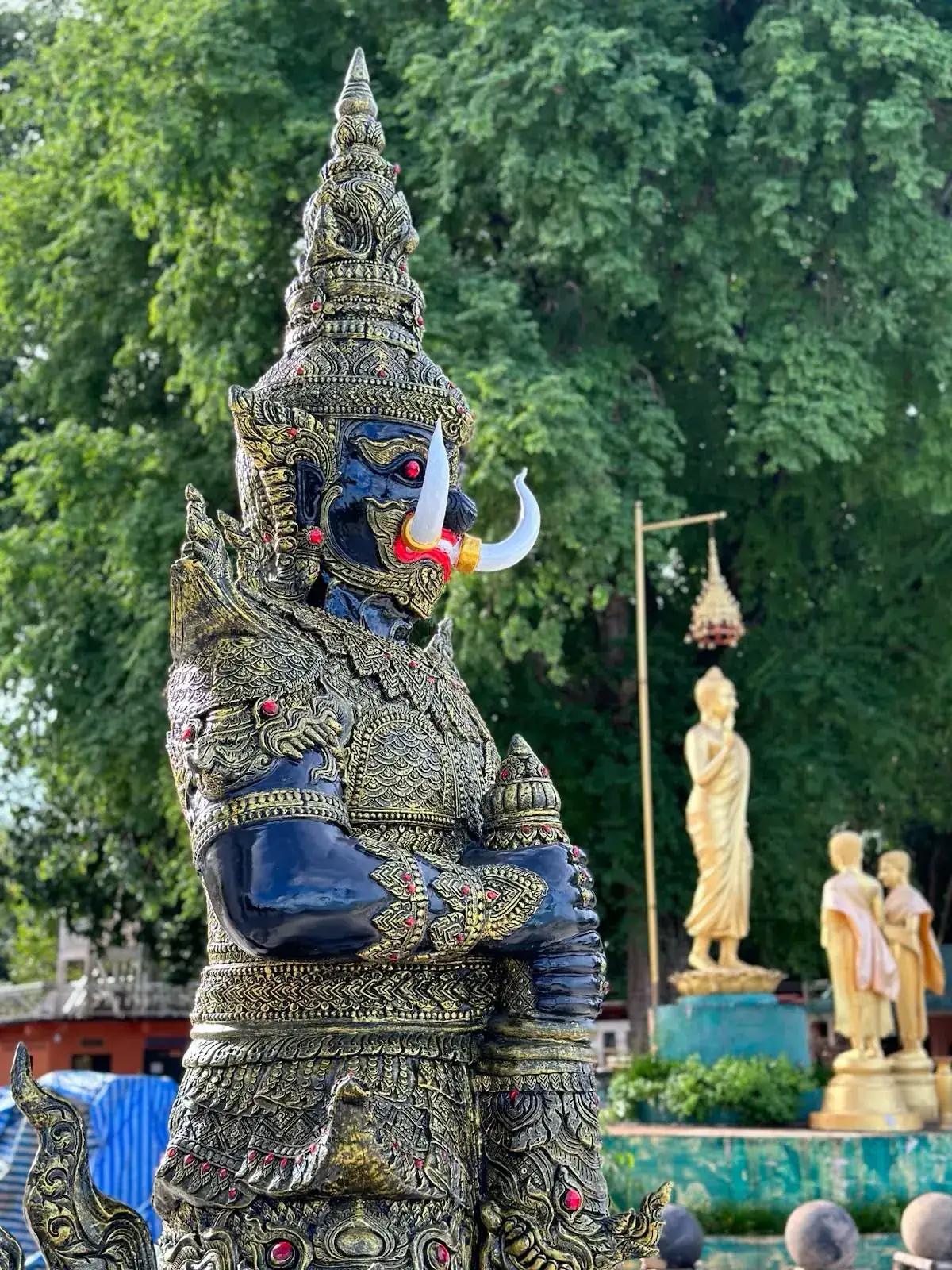 Detailed Yaksha statue with golden Buddha figures in the background at Wat Koh Mak