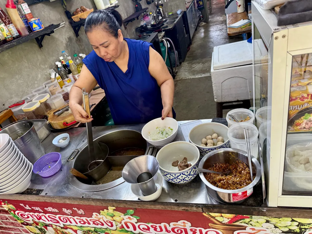 Cook preparing noodle soup with fresh toppings at Mong Kitchen in Ao Kao, Koh Mak