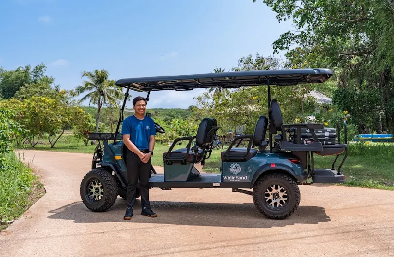 White Sand Resort staff member next to a teal six-seater golf cart on a Koh Mak road