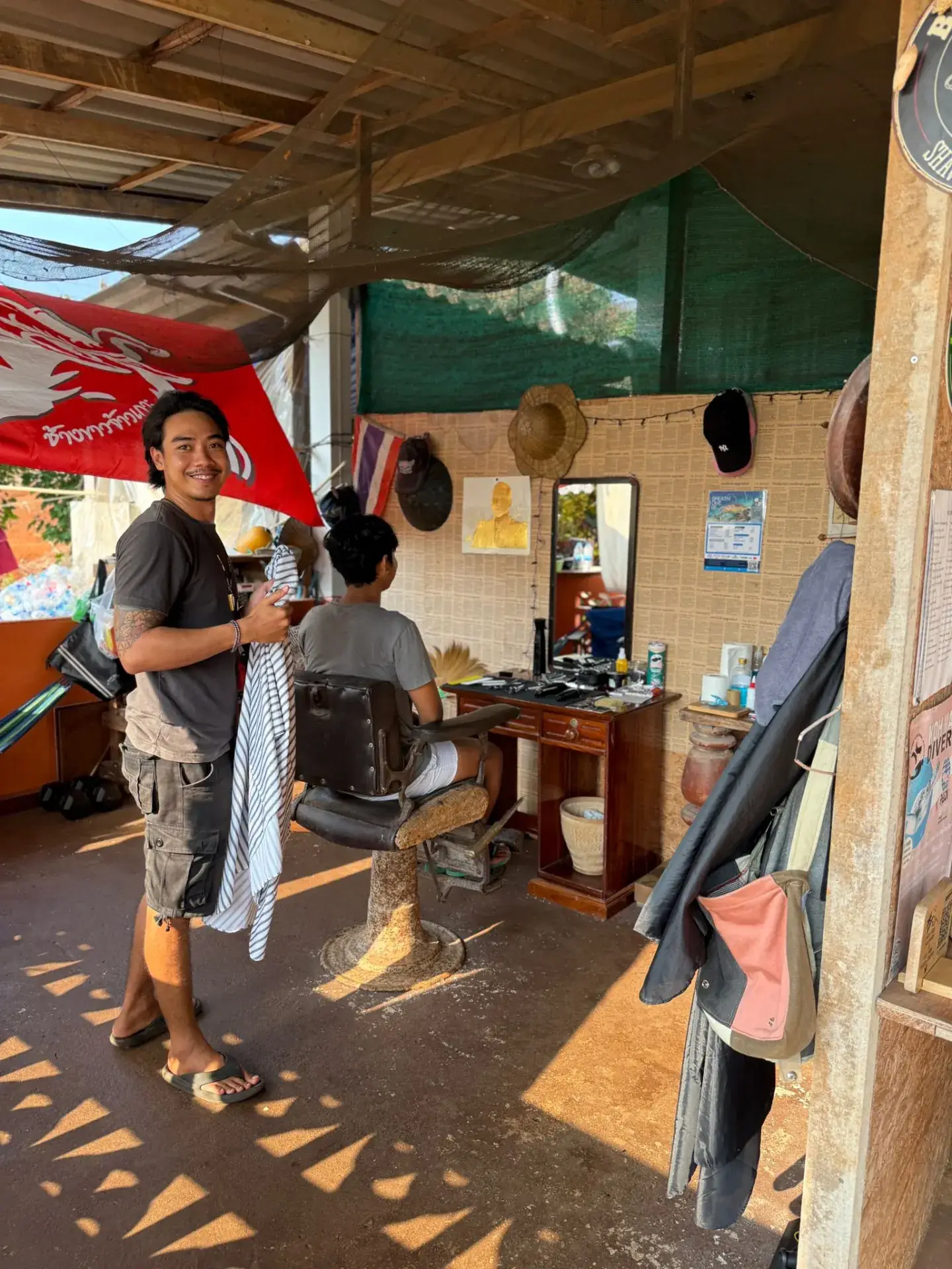 Local barber cutting hair in a traditional open-air shop on Koh Mak