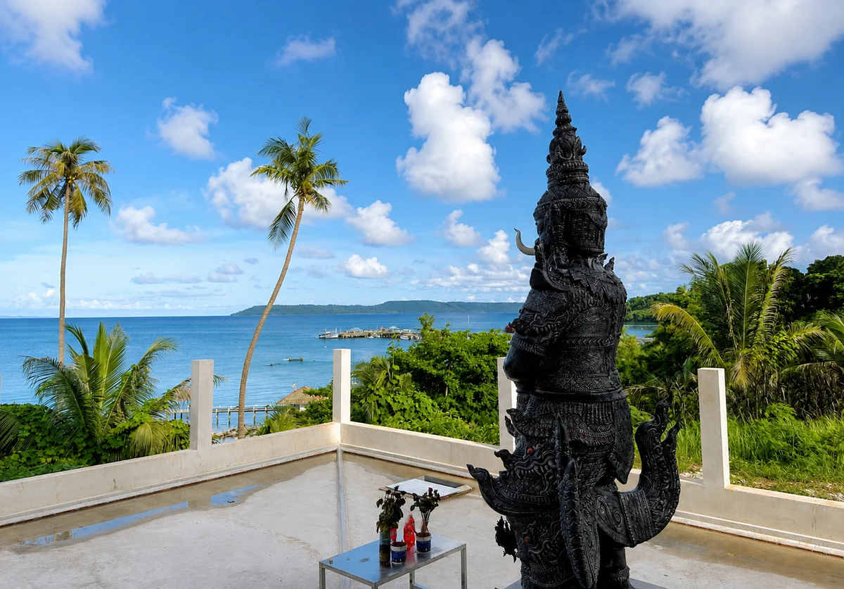 Ornate black Yaksha guardian statue overlooking Ao Nid pier and the turquoise sea at Wat Koh Mak, Thailand
