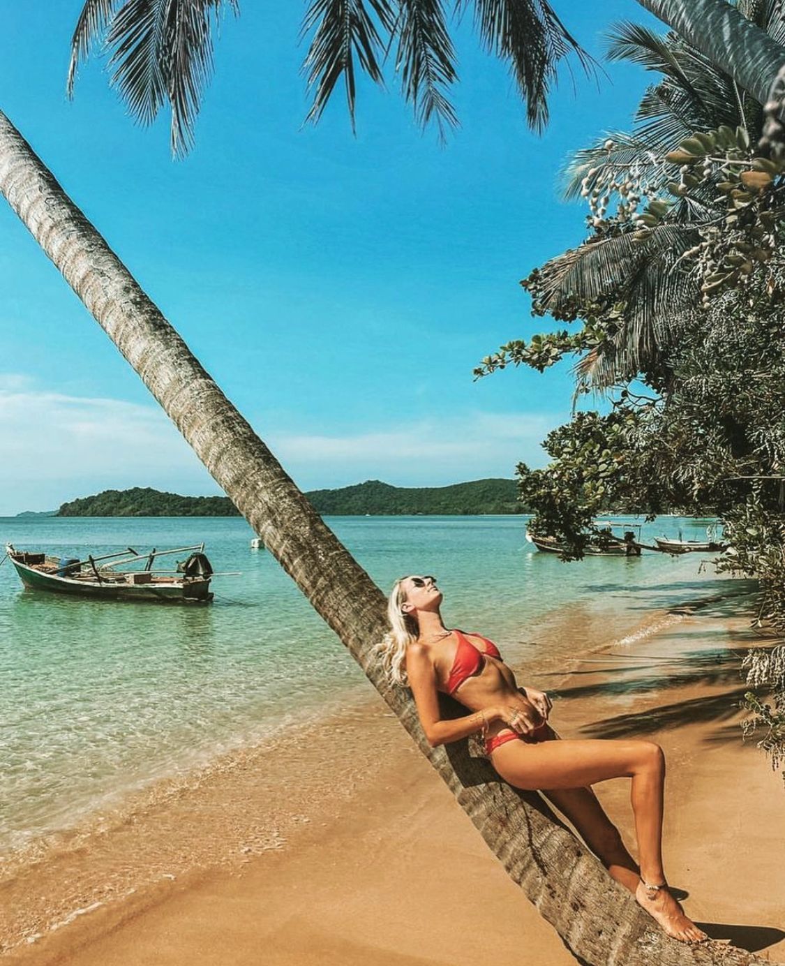 Woman relaxing against a leaning coconut palm on a Koh Mak beach