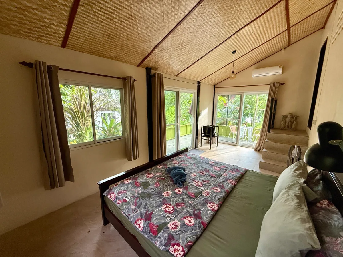 Bright bedroom interior with woven ceiling, floral bedding and garden views through sliding doors at Rambutan House, Koh Mak