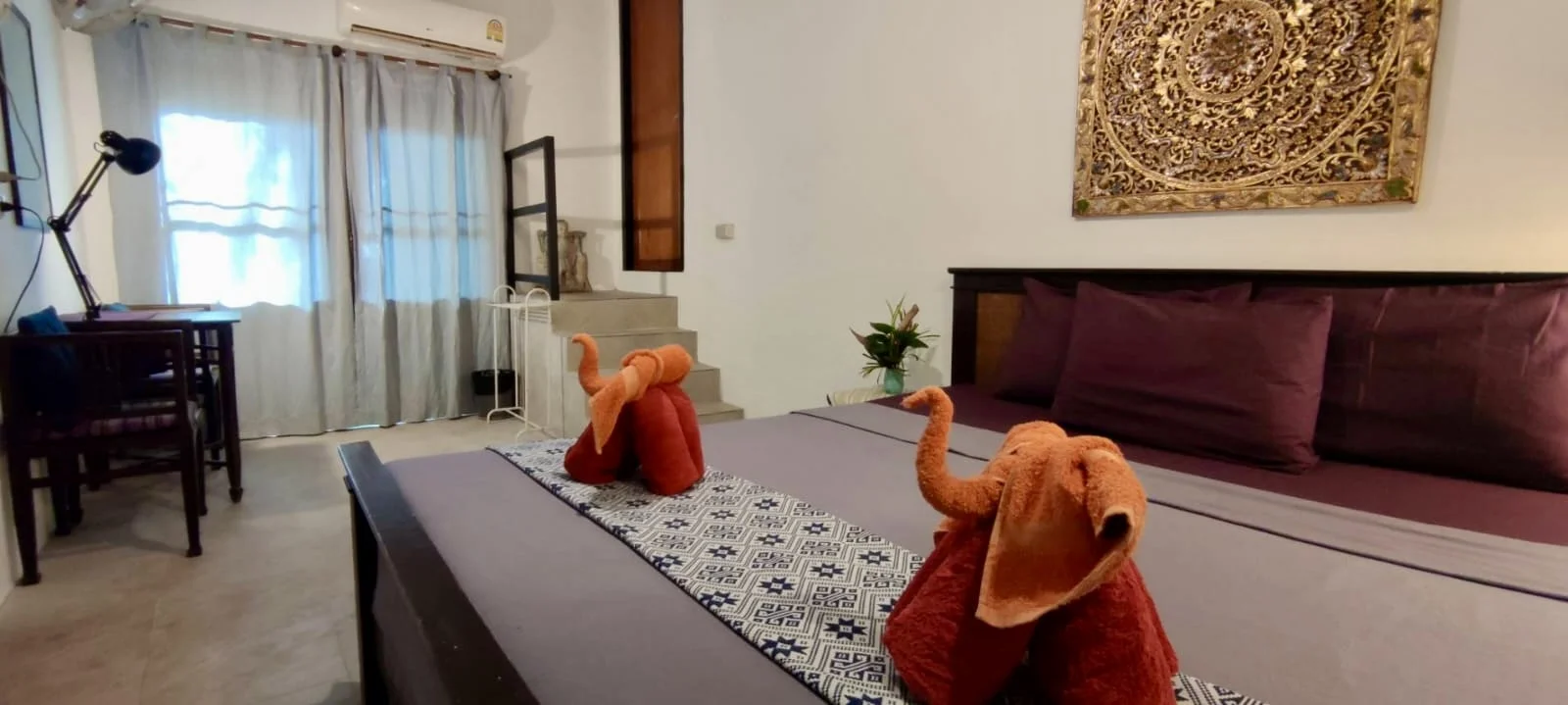 Bedroom detail with elephant-shaped towels, carved Thai wall art and a working desk at Rambutan House, Koh Mak