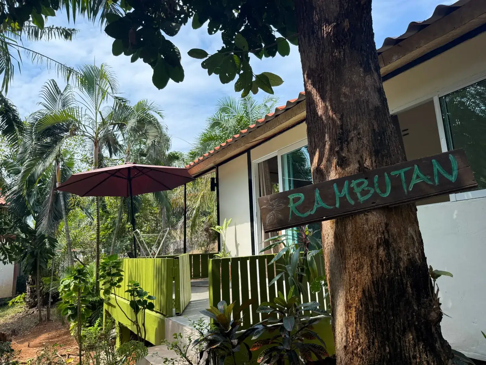 Rambutan House exterior with hand-painted wooden sign, green terrace fence and palms on Koh Mak, Thailand