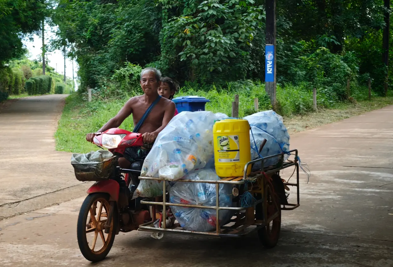 Local man on a motorbike sidecar loaded with bags of used plastic bottles for recycling on a green roadside on Koh Mak
