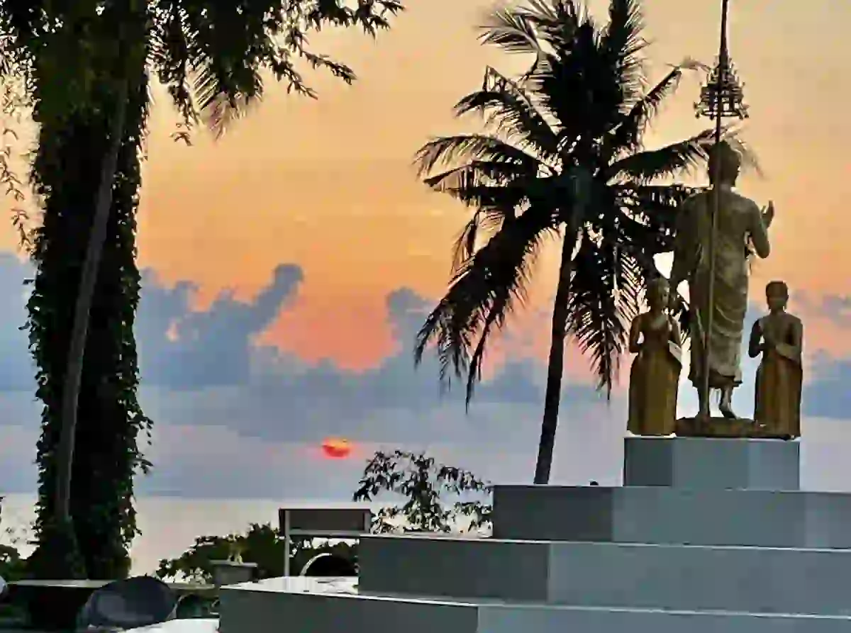 Golden Buddha statues silhouetted against a colourful sunset on Koh Mak