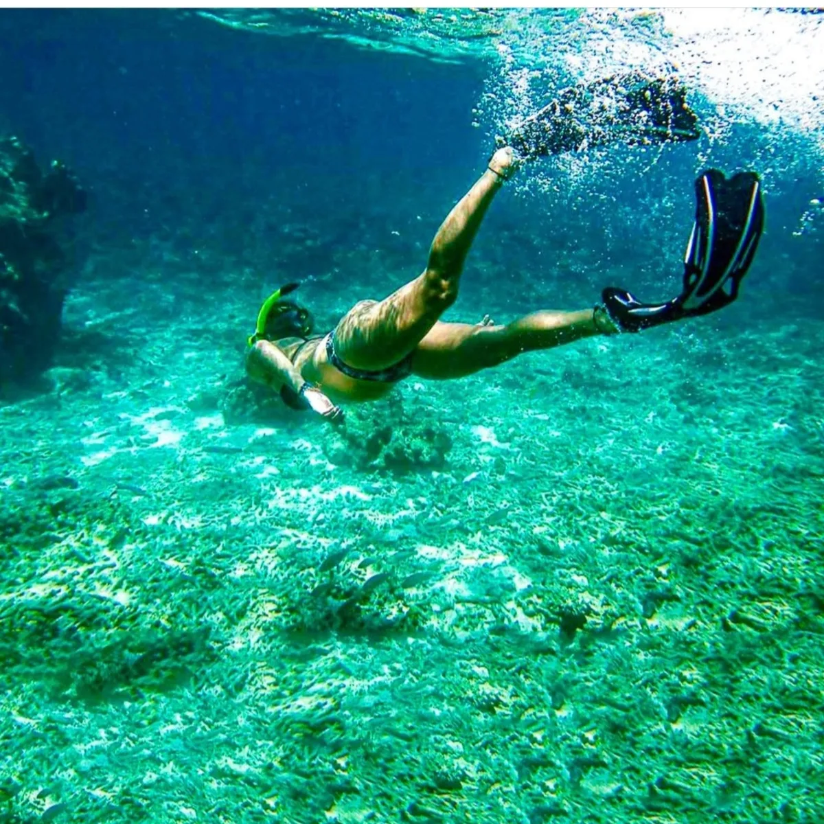 Snorkeler swimming over a coral reef in clear turquoise water off Koh Mak
