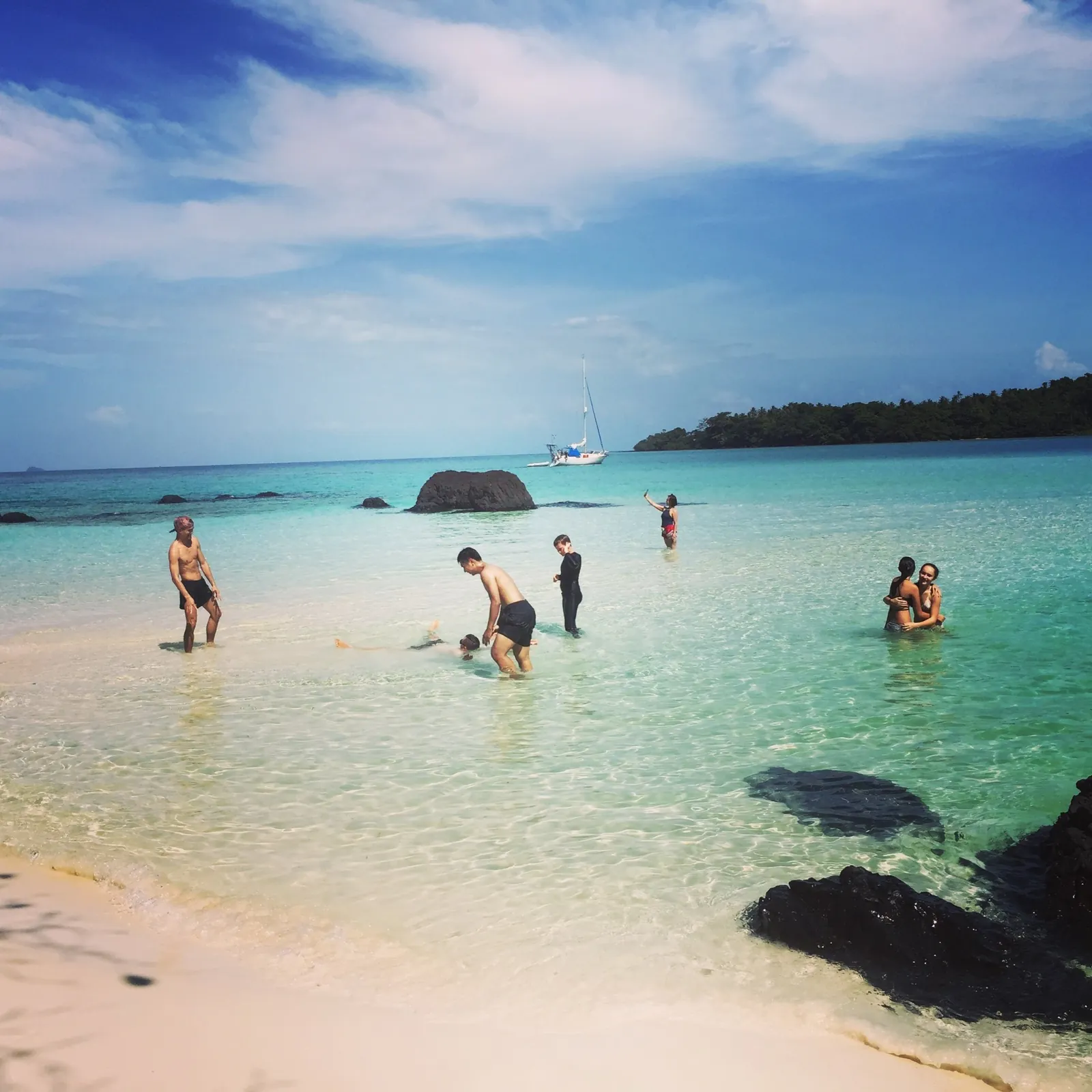 Swimmers and snorkelers in clear turquoise water with a sailboat anchored off Koh Kham