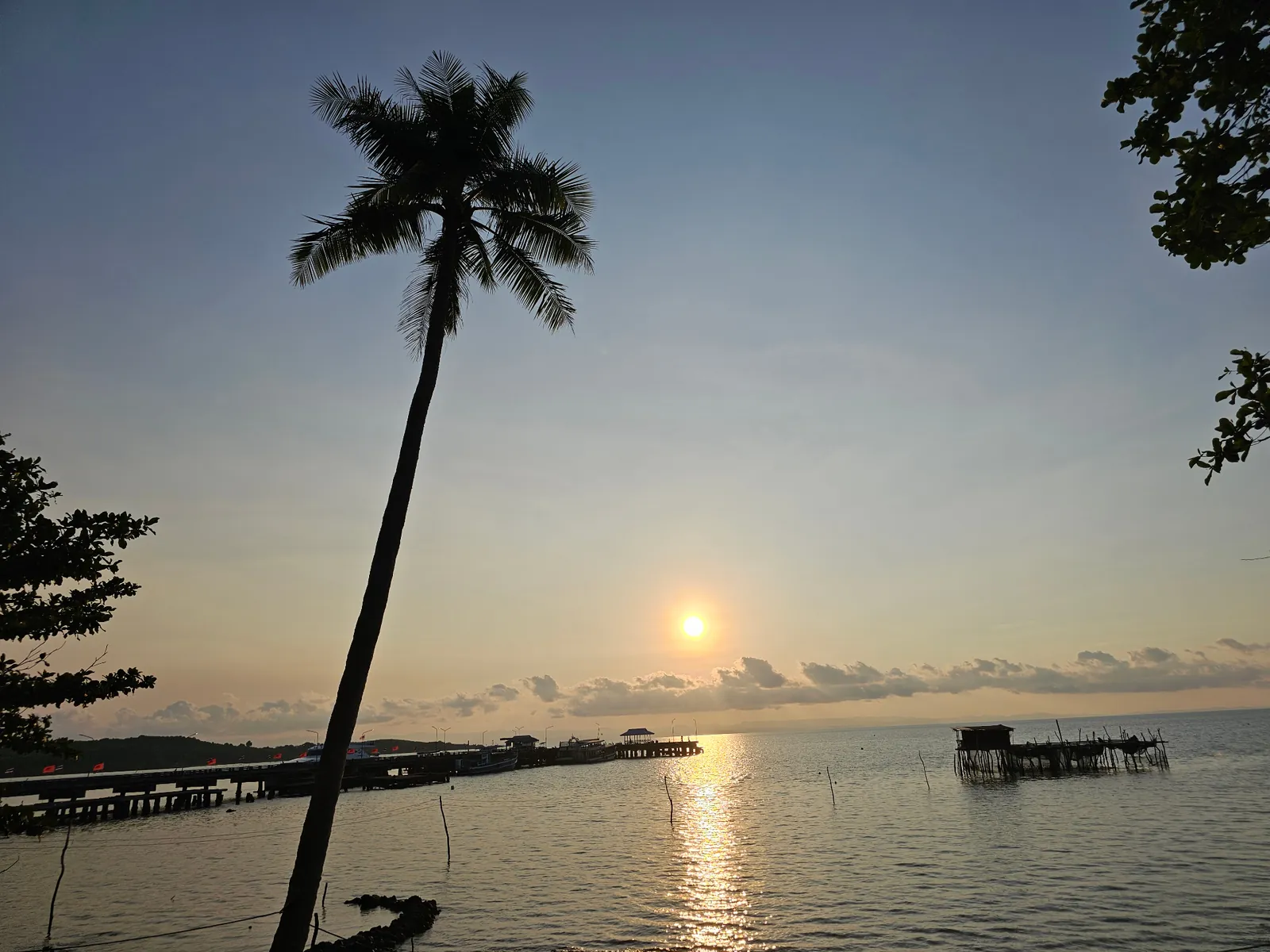 Sunset over the Ao Nid pier with a tall palm silhouette, Koh Mak