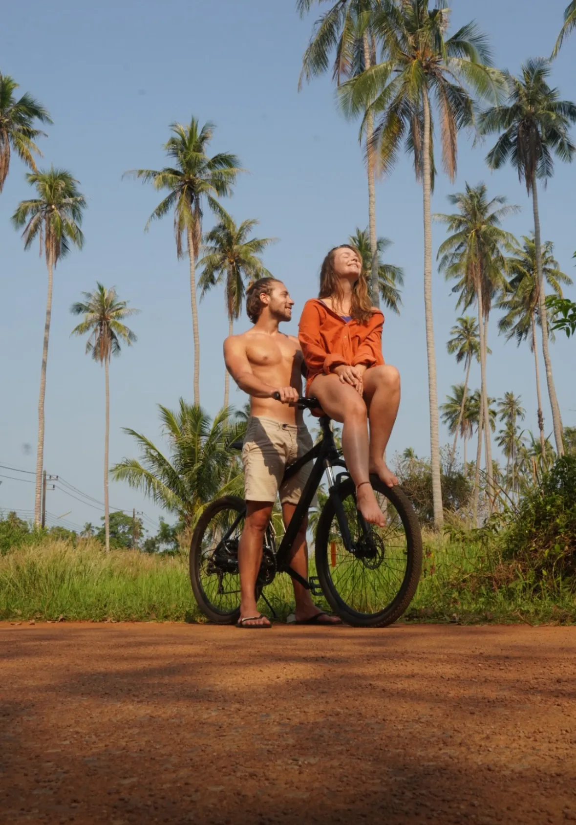 Couple with a bicycle on a quiet palm-lined road on Koh Mak