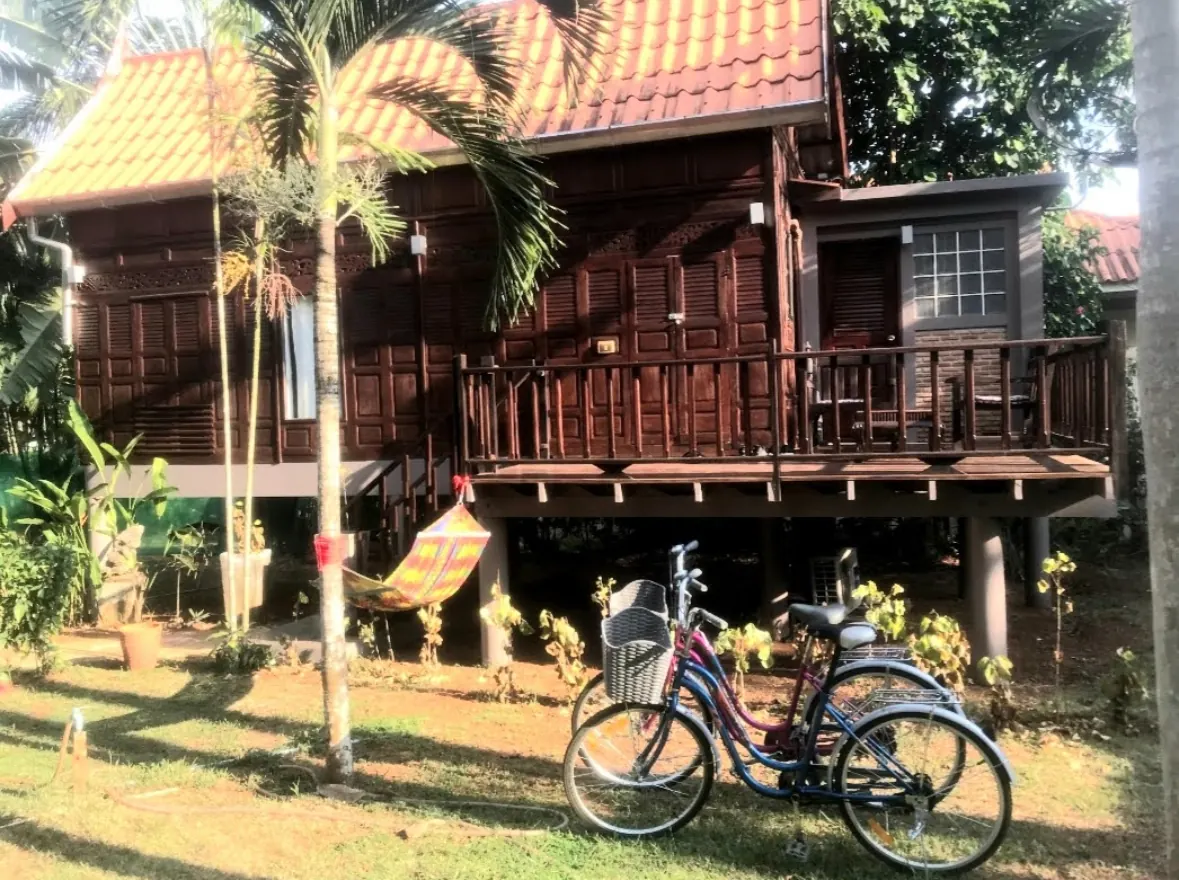 Traditional Thai-style wooden bungalow on stilts with a colourful hammock and bicycles in a tropical garden on Koh Mak