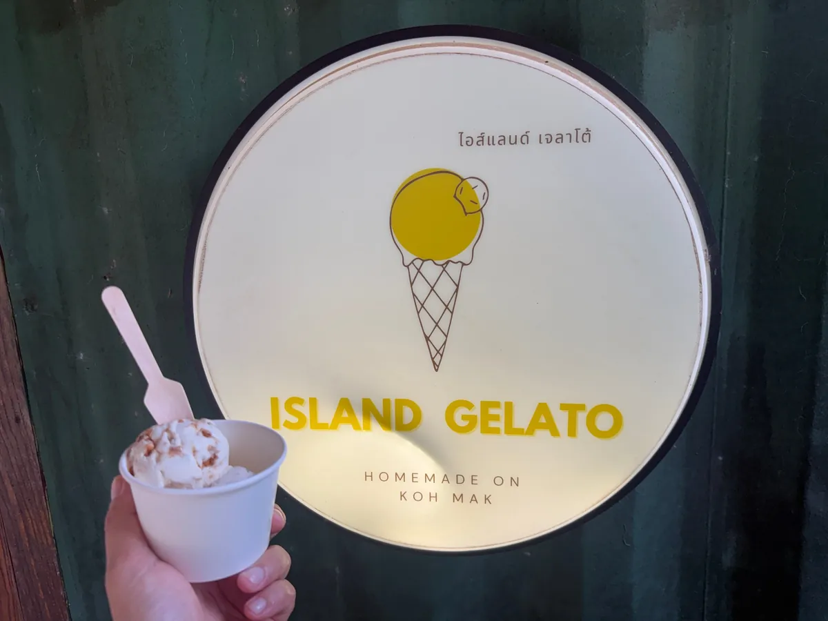 Cup of homemade Island Gelato ice cream in front of the shop's round sign on Koh Mak