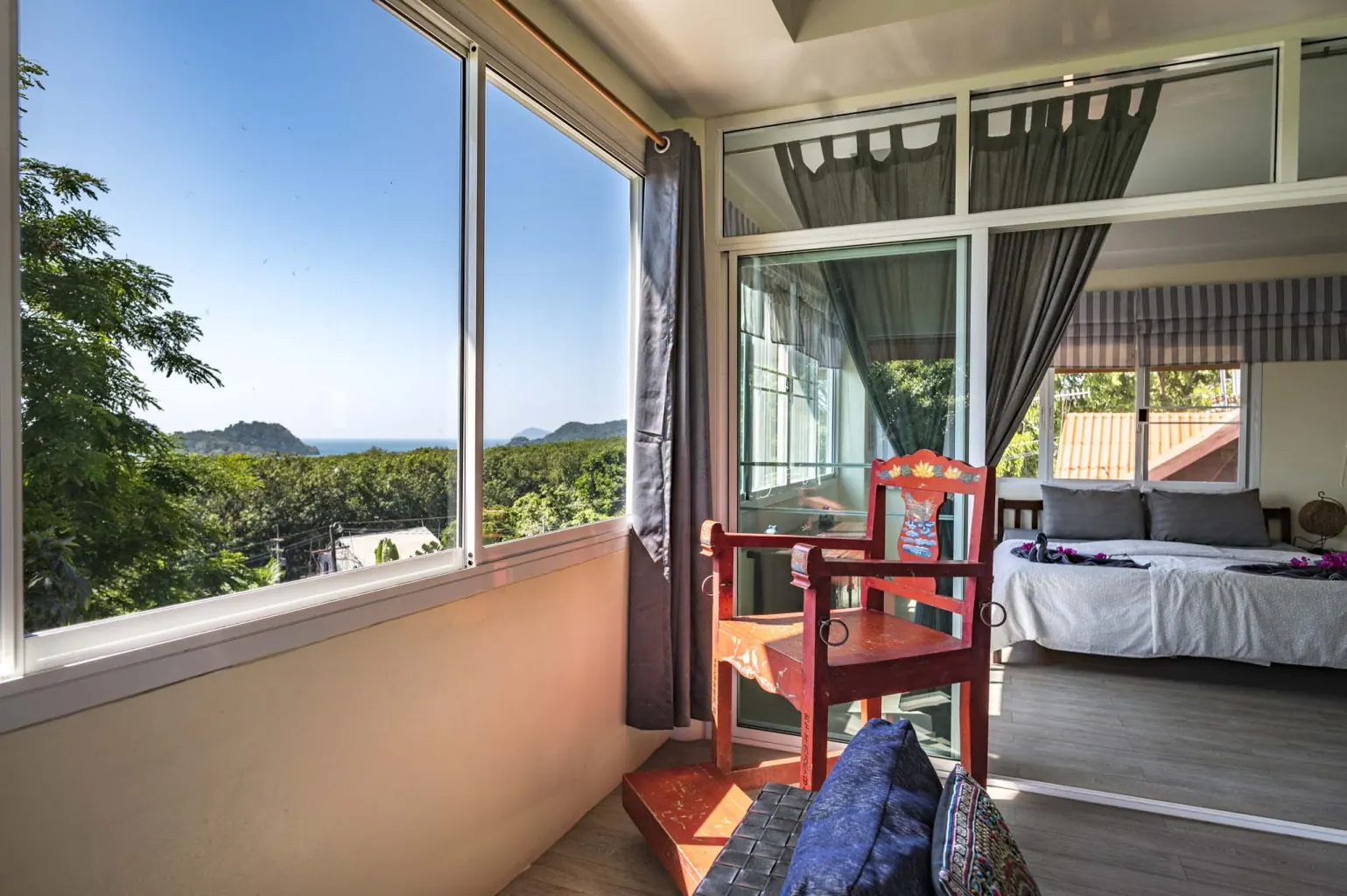 Panoramic sea view from The Penthouse Koh Mak bedroom with carved red Thai chair and tropical treetops, Koh Mak, Thailand