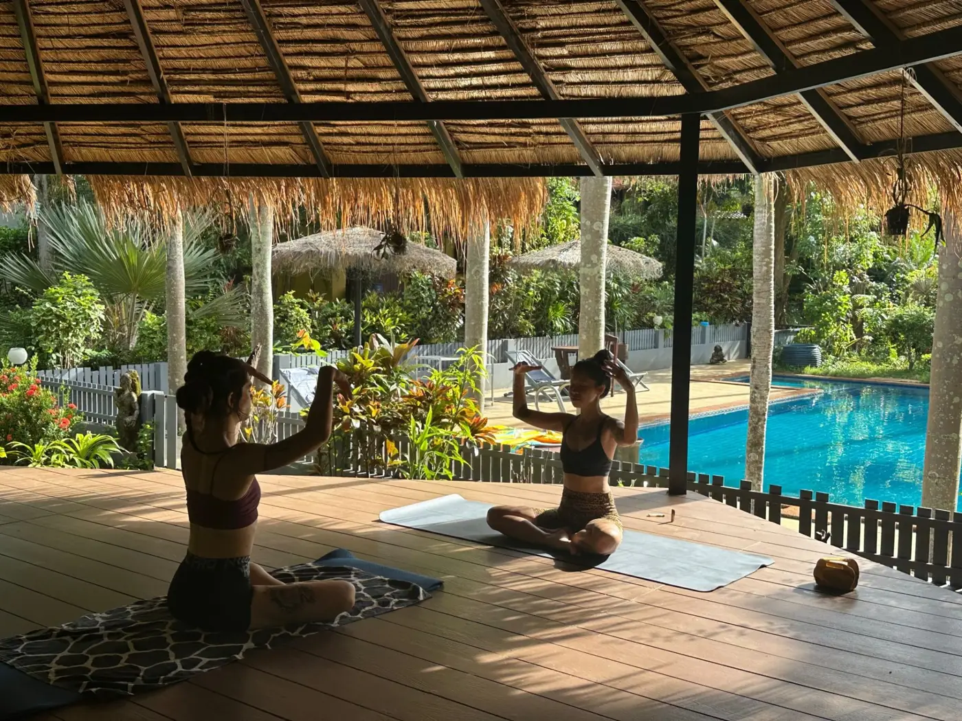 Two women practicing yoga in a thatched pavilion beside the pool on Koh Mak