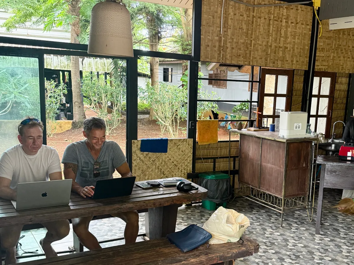 Two guests working on laptops at the open-air Panthera Protein Kiosk & Café, surrounded by tropical greenery and woven bamboo walls