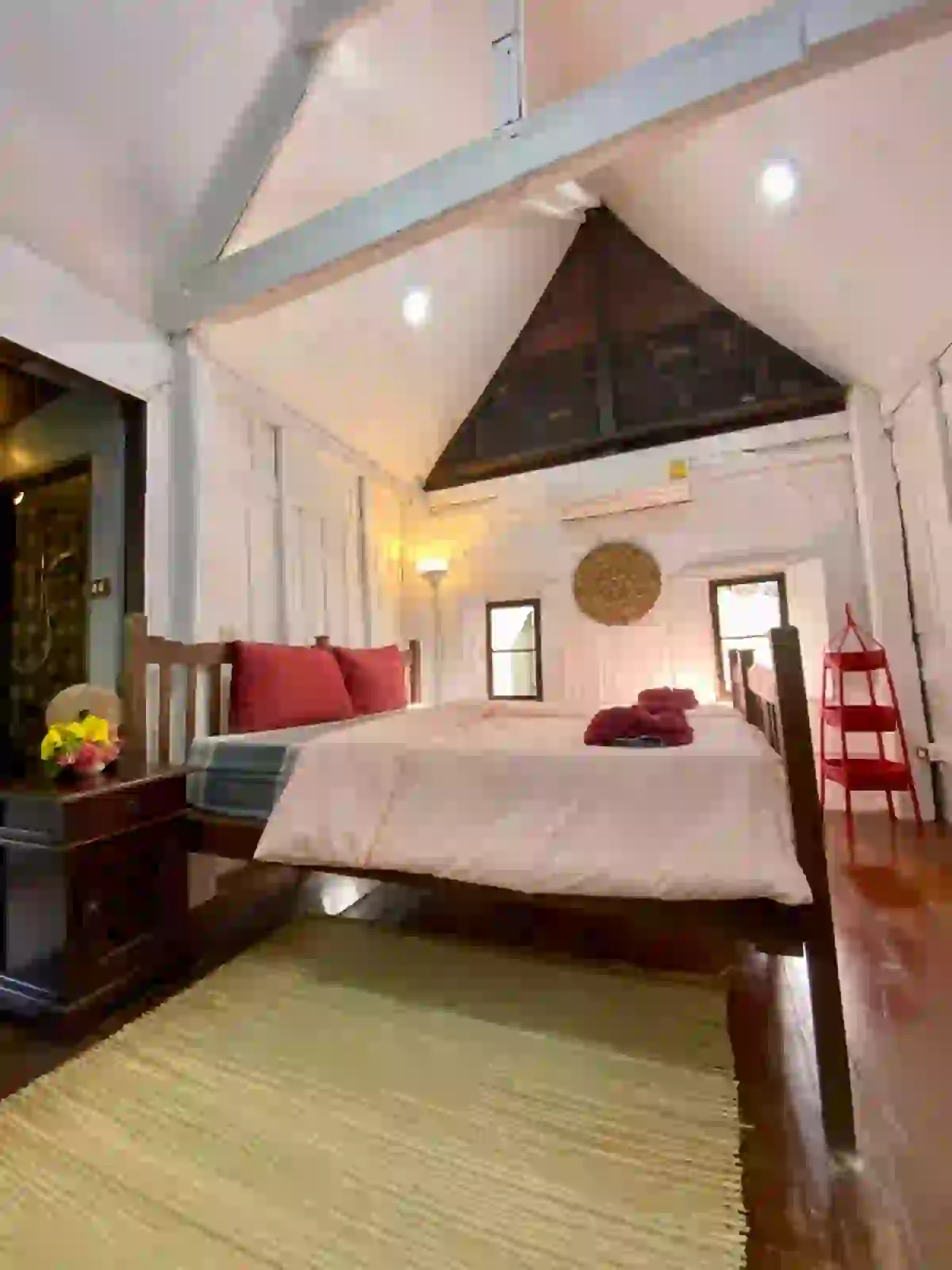 Traditional Thai wooden bedroom interior with red cushions, carved details and woven mat at Koh Mak Village