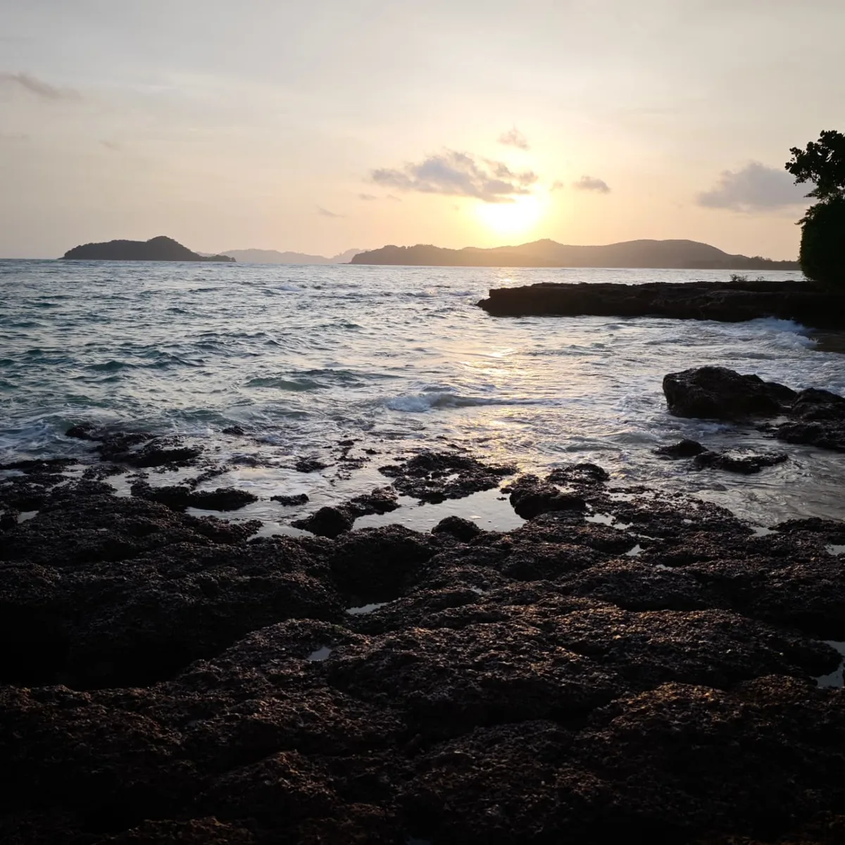 Sunset over a rocky shoreline with gentle waves and distant islands on Koh Mak