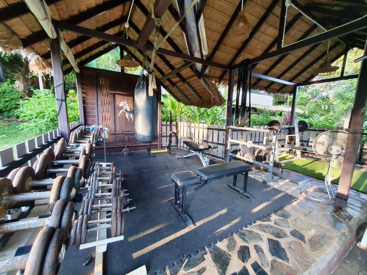 Open-air outdoor gym with dumbbells, benches and a punching bag under a thatched roof on Koh Mak