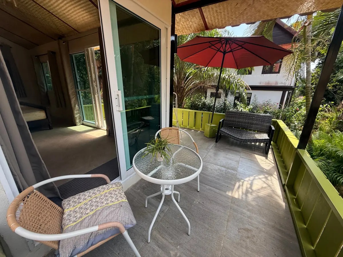 Private terrace with outdoor seating, red umbrella and green garden fence at Rambutan House, Koh Mak